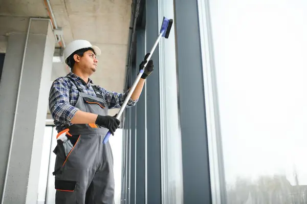 Male professional cleaning service worker cleans the windows and shop windows of a store with special equipment.