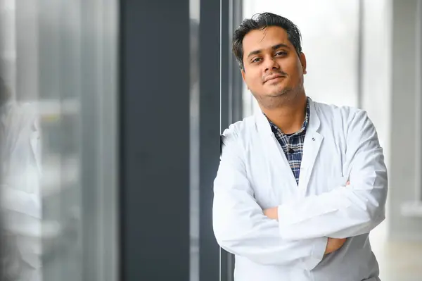 Portrait of male indian doctor on clinic corridor as background