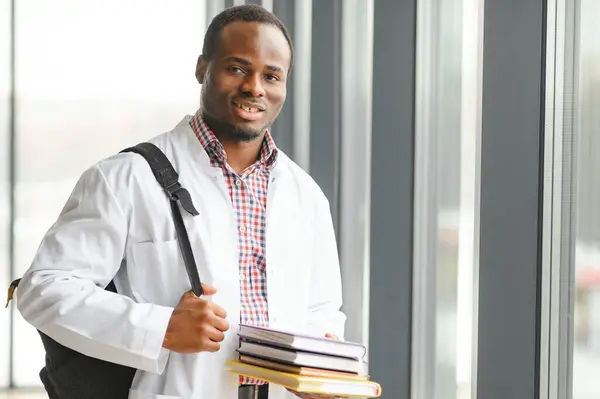 Black male doctor student wearing a lab coat with book.