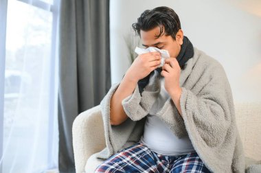Hasta adam oturma odasında kanepede oturuyor, hapşırmanın alerjisi ve burnu akıyor, peçeteli Hintli adamın soğuk algınlığı var..