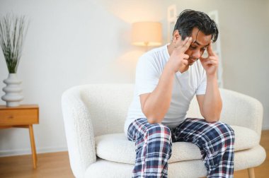 Hoşnutsuz Hintli adam baş ağrısı problemini tedavi etmek için tapınakları ovuyor, tansiyon ve migrenden muzdarip, evde acı içinde kıvranan yüksek tansiyon. Hintli adam kanepede. Yaşam Tarzları