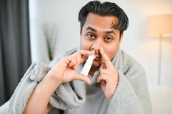 A sick Indian is treated at home and uses a nasal spray. Healthcare concept.