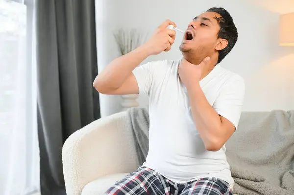 Indian man sick at home, cold, flu. A man uses a throat spray.