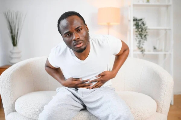 Black Man Having Stomachache Suffering From Painful Abdominal Spasm Standing Touching Aching Abdomen At Home. Abdomen Pain, Stomach Inflammation And Appendicitis Concept