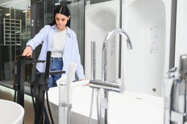 Genç bir kadın, tesisat dükkanında bir sürü hijyenik eşya bulunan yeni banyo mobilyalarını seçiyor..