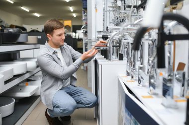 Adam inşaat süpermarketinde banyo musluğu seçiyor, evdeki su tesisatını tamir ediyor..