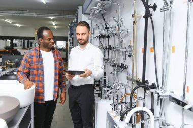 Muslukları seçen Afrikalı genç bir adam su tesisatı dükkanının yanında satıcıyla duruyor..