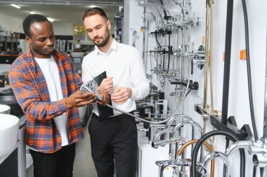 Muslukları seçen Afrikalı genç bir adam su tesisatı dükkanının yanında satıcıyla duruyor..