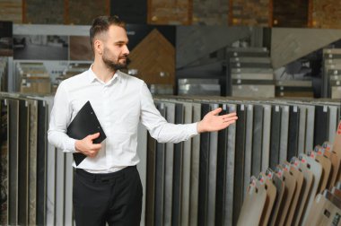 Seramik seramik satıcısının portresi. Satıcı geniş bir fayans çeşidinin arka planında duruyor..