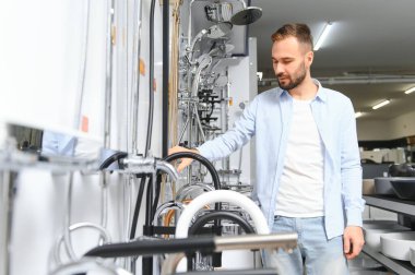 Tesisat bölümündeki nalbur dükkanındaki bir müşteri mutfak için musluk seçiyor..