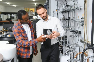 Muslukları seçen Afrikalı genç bir adam su tesisatı dükkanının yanında satıcıyla duruyor..