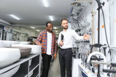 Muslukları seçen Afrikalı genç bir adam su tesisatı dükkanının yanında satıcıyla duruyor..