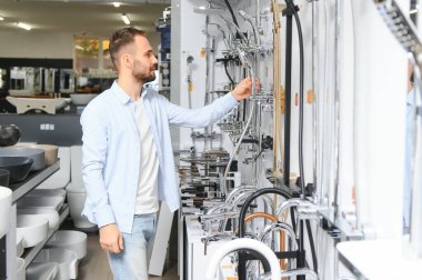 Tesisat bölümündeki nalbur dükkanındaki bir müşteri mutfak için musluk seçiyor..