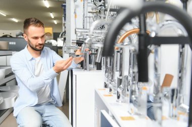 Tesisat bölümündeki nalbur dükkanındaki bir müşteri mutfak için musluk seçiyor..