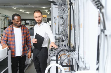 Muslukları seçen Afrikalı genç bir adam su tesisatı dükkanının yanında satıcıyla duruyor..