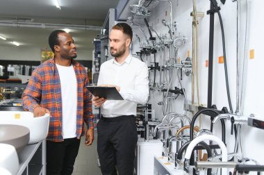 Muslukları seçen Afrikalı genç bir adam su tesisatı dükkanının yanında satıcıyla duruyor..