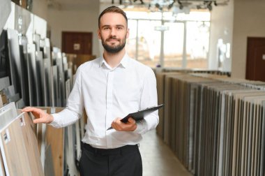 Seramik seramik satıcısının portresi. Satıcı geniş bir fayans çeşidinin arka planında duruyor..