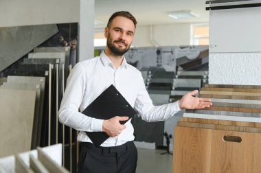 Seramik seramik satıcısının portresi. Satıcı geniş bir fayans çeşidinin arka planında duruyor..