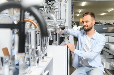 Tesisat bölümündeki nalbur dükkanındaki bir müşteri mutfak için musluk seçiyor..