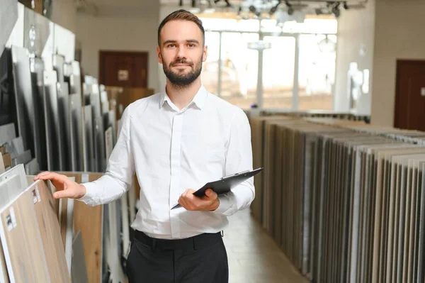 Seramik seramik satıcısının portresi. Satıcı geniş bir fayans çeşidinin arka planında duruyor..