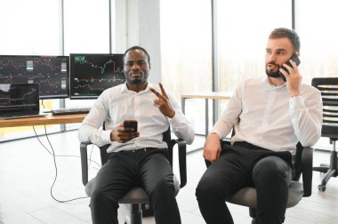 İki güler yüzlü iş adamı, finans analisti veya yatırım danışmanı ellerinde laptop ve belgelerle ofiste oturuyorlar, iş analizi, danışmanlık hizmetleri, takım portresi