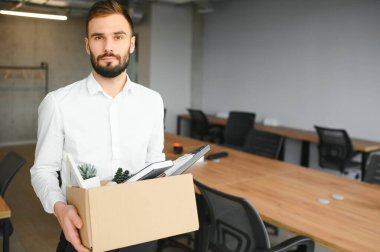 Man by dismissal. Guy lost job. Fired manager in company. Dismissal box in hands of employee. Man office worker disappointed by dismissal. Fired male in blurred office. Discharge company employees