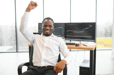 Afro-Amerikalı borsacı, çalışma istasyonu ve analiz teknolojisi kullanarak ofiste çalışıyor..