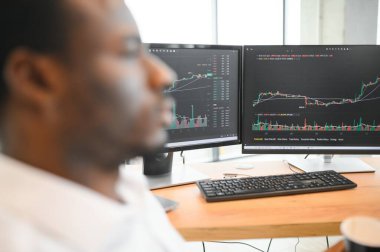 Afro-Amerikalı borsacı, çalışma istasyonu ve analiz teknolojisi kullanarak ofiste çalışıyor..