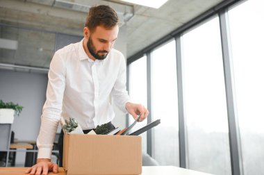 Man by dismissal. Guy lost job. Fired manager in company. Dismissal box in hands of employee. Man office worker disappointed by dismissal. Fired male in blurred office. Discharge company employees