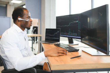 Afro-Amerikalı borsacı, çalışma istasyonu ve analiz teknolojisi kullanarak ofiste çalışıyor..