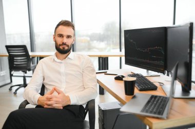 Kripto tüccarı iş yerinde elinde çizelgelerle monitörün önünde oturuyor.