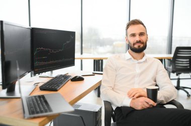 Kripto tüccarı iş yerinde elinde çizelgelerle monitörün önünde oturuyor.