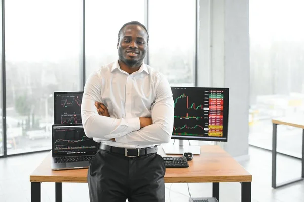 African-American broker works in office using workstation and analysis technology.