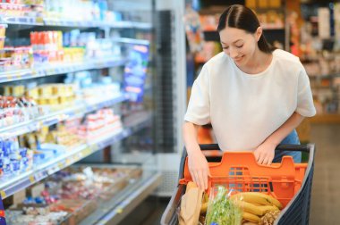 Markette ürünlere bakan mutlu genç bir kadın. Gülümseyen kadın süpermarkette alışveriş yapıyor.