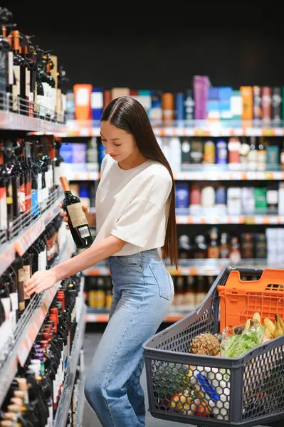 girl chooses wine in supermarket.