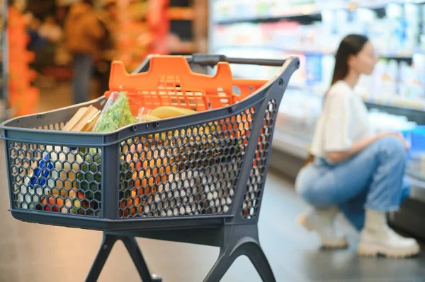A full basket of products in a supermarket on the background of a young woman.