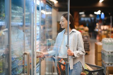 Market alışverişi. Süpermarkette Trolley Cart 'a yaslanan Gülümseyen Mutlu Kadın Portresi.