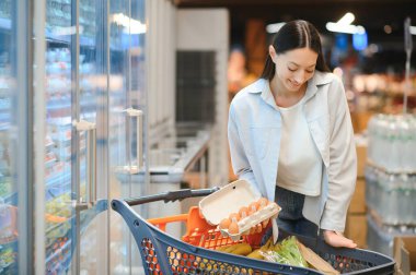20 'li yaşlarda mutlu, genç bir kadın süpermarketten alışveriş yapıyor..
