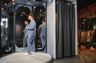 Erkek giyim mağazasında aynada takım elbise deneyen gülümseyen adam..