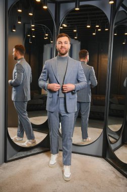 Erkek giyim mağazasında aynada takım elbise deneyen gülümseyen adam..