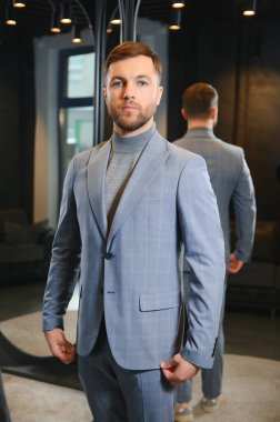 Erkek giyim mağazasında aynada takım elbise deneyen gülümseyen adam..