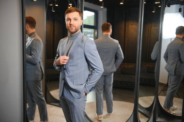 Erkek giyim mağazasında aynada takım elbise deneyen adam..