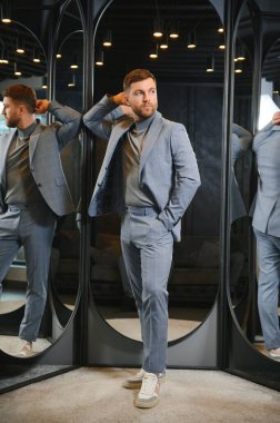 Modern genç yakışıklı işadamı kravat takım elbise dükkanda duran aynanın önünde ayarlama Klasik takım elbise giymiş.