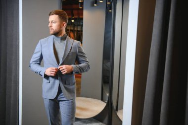 Modern genç yakışıklı işadamı kravat takım elbise dükkanda duran aynanın önünde ayarlama Klasik takım elbise giymiş.