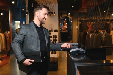 Yeni kıyafetler ve ayakkabılarla dolu kutular taşıyan ve telefonla ödeme yapan mutlu müşteriler..