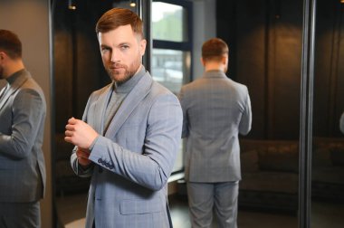 Modern genç yakışıklı işadamı kravat takım elbise dükkanda duran aynanın önünde ayarlama Klasik takım elbise giymiş.