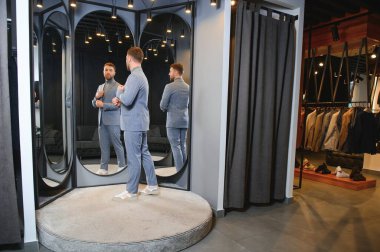 Modern genç yakışıklı işadamı kravat takım elbise dükkanda duran aynanın önünde ayarlama Klasik takım elbise giymiş.