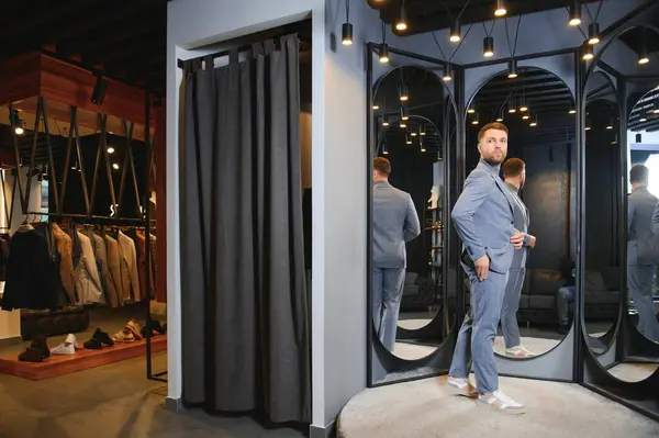 Erkek giyim mağazasında aynada takım elbise deneyen adam..