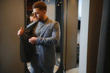 Modern genç yakışıklı işadamı kravat takım elbise dükkanda duran aynanın önünde ayarlama Klasik takım elbise giymiş.