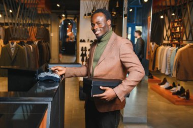 Kutular dolusu yeni kıyafet ve ayakkabı taşıyan ve kredi kartıyla ödeme yapan mutlu müşteriler..